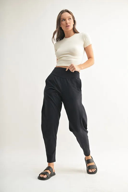 Woman modeling MONO B Flowbarrel High Waist Active Pants in black with a fitted top and sandals.
